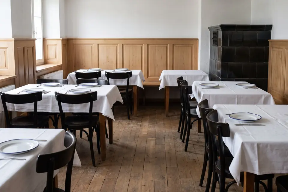 Die Gaststube: Täfer, Kachelofen und gedeckte Tische mit weissem Leinen