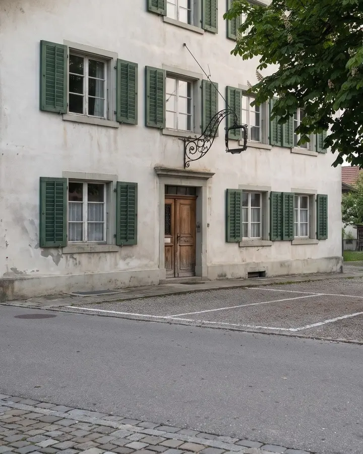 Die Hausfront mit den grünen Läden und den Parkplätzen davor
